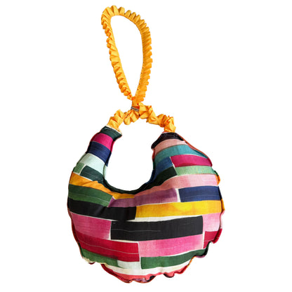 A crescent-shaped shoulder bag made of colorful patchwork fabric strips, featuring a bright yellow crinkled fabric handle, shown against a plain white background.