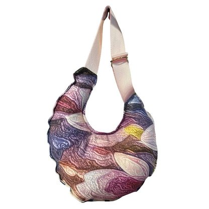 A crescent-shaped shoulder bag with a multicolor abstract marbled pattern in purple, pink, blue, and brown, featuring a wide beige shoulder strap.